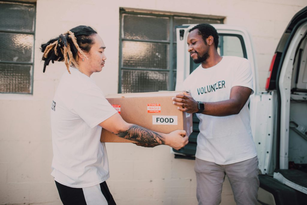 Two volunteers transferring a food box from a van, symbolizing community support and charity work.